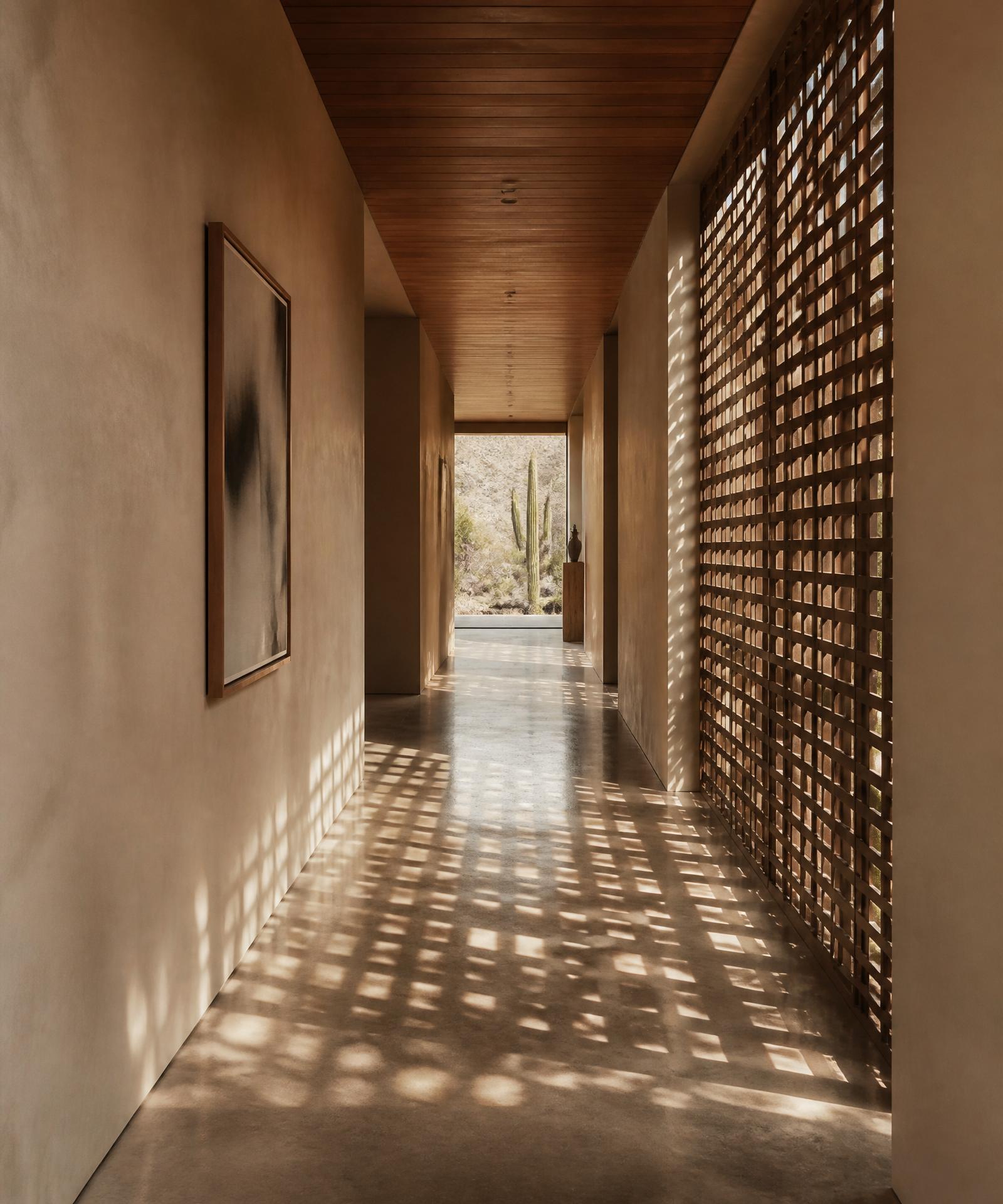 A long gallery corridor inside a Scottsdale desert modern home with polished concrete floor, plaster walls, a wooden ceiling, and afternoon sunlight cast through a perforated bronze screen throwing a grid of rectangular shadows down the corridor floor, one framed piece of art on the wall